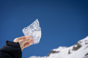 A beautiful piece of ice in a female hand against the blue sky and mountains