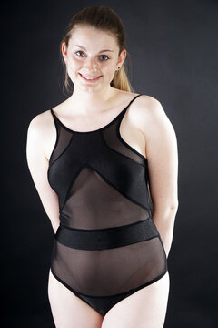 Cheerful happy smiling woman wears black body suit as lingerie or underwear in studio in front of black background
