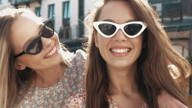 Two young beautiful smiling hipster female in trendy summer sundress. Sexy carefree women posing on the street background in sunglasses. Positive models having fun and going crazy