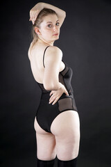 Beautiful young woman wears black body suit as lingerie or underwear in studio in front of black...