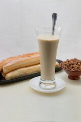 Close up of a table with a glass of horchata, a plate full of fartons and a bowl of tiger nuts