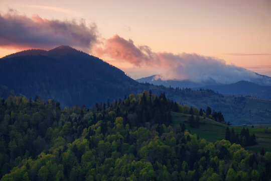 carpathian rural area in spring at sunset. mountainous scenery with forested hills beneath a cloudy sky. nature background in evening light