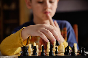 A chessboard with spaced figures, in the background a boy out of focus. Education concept, intellectual game.