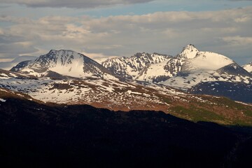Fototapeta na wymiar Scenic view of a snowy mountain range near Sjoholt, Norway against green hills on a cloudy day