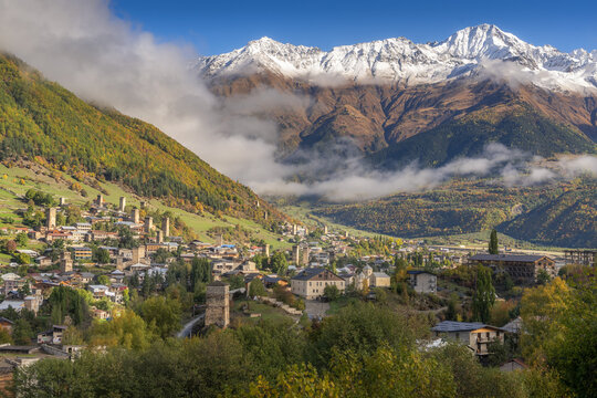 Svan towers in Mestia village with snow mountain range background in sunny day during autumn period