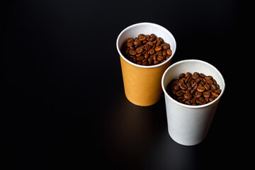 Two paper cups filled with grains of coffee on black background.