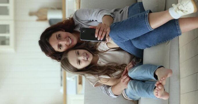Happy excited mom and cute little daughter child watching online content on mobile phone, talking on video call, looking at cellphone screen, speaking, smiling, laughing