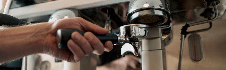 Close-up of male hand holding portfilter near coffee grinder, picking up ground coffee