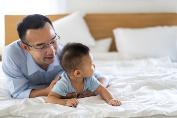 Portrait of enjoy happy love family asian father playing with adorable little asian baby.newborn, infant.dad touching with cute son moments good time in a white bedroom.father day, Love of family