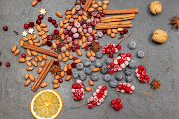 Cinnamon sticks, nuts, frozen berries and orange chips. Black background.