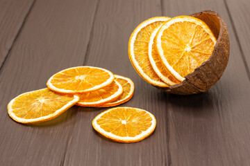 Slices of dried orange are scattered on the table. Orange chips in a coconut shell.