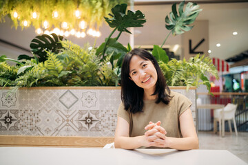 Smiling beautiful asian woman sitting in cafeteria at shopping mall.