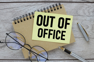 out of office. text on a yellow sticky note on the desk next to the glasses.
