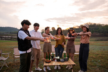 Group of young Asian people are enjoy camping , playing sparkler in natural campsite at twilight