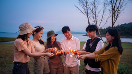 Group of young Asian people are enjoy camping , playing sparkler in natural campsite at twilight