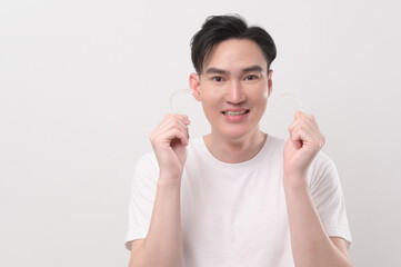 Young smiling man holding invisalign braces over white background studio, dental healthcare and Orthodontic concept...