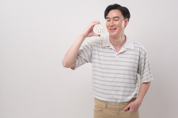 Young smiling man holding small model house over white background studio..