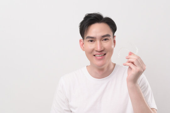 Young smiling man holding invisalign braces over white background studio, dental healthcare and Orthodontic concept...