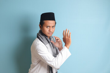 Portrait of Asian muslim man in white koko shirt doing martial arts gesture or pencak silat. Isolated image on blue background