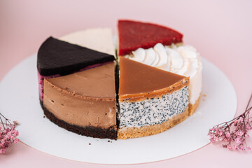 Cake from different pieces of cheesecake with different flavors on pink background with dried flowers.