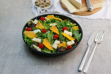 fresh green salad with brie cheese on black plate on grey table 
