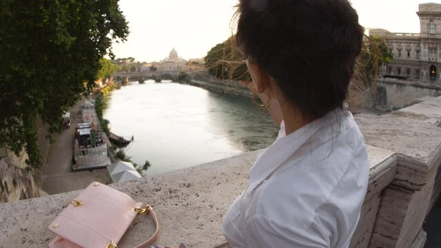 Young woman taking pictures from a bridge on river tiber in Rome. View of St. Peter and Vatican city, Italy.