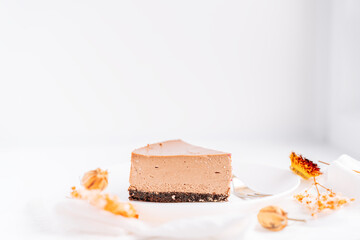 Chocolate cheesecake on plate with fork against white background with dried flowers.