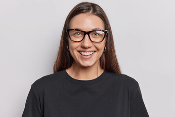 Portrait of cheerful dark haired woman glad to get new job smiles pleasantly has perfect even teeth wears optical eyeglasses and casual black t shirt isolated over white background. Happy emotions
