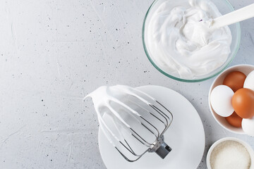 Whipped egg whites - whipped Italian meringue on a wire whisk, eggs, sugar, on a gray background. copy space.