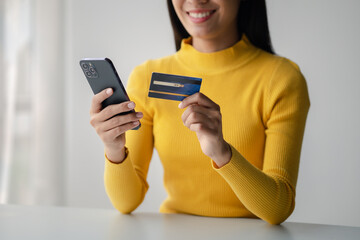 Naklejka premium Beautiful woman holding a credit card, she uses a credit card to pay for goods and services online, the concept of using a credit card for online shopping, ordering goods and services on the website.