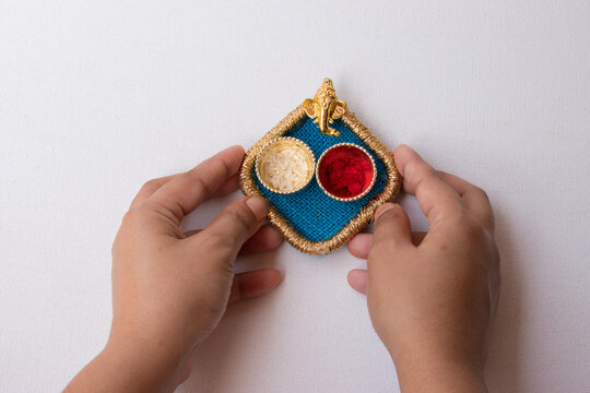 Hand holding beautiful small thali having God Ganesh face and red roli and chawal means tika and rice in white background. It is used for any hindu festival like Rakshbandhan, diwali, durga puja.