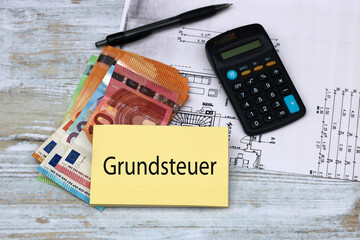 Konzept der deutschen Grundsteuer. Bauplan mit Taschenrechner und Eurobanknoten. Auf einem...