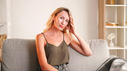 Fototapeta premium Upset situation. Regretful woman. Disappointed mood. Sad lady feeling sorrow leaning head sitting sofa in light room interior.