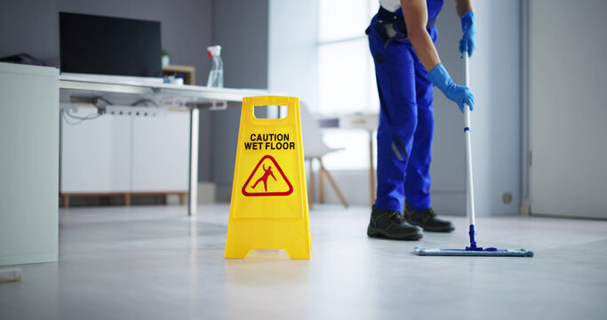 Male Janitor Cleaning Floor With Caution Wet Floor Sign