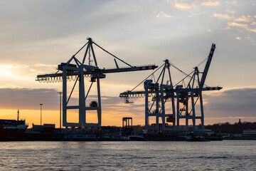 Fototapeta na wymiar The busy harbour of Hamburg showing a skyline of cranes and container ships at sunset 