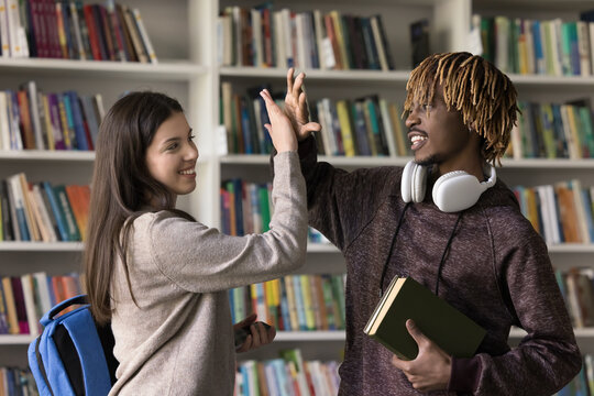 Multinational cheerful students, African and Caucasian schoolmates giving high five, celebrate end of session successfully, pass exam, get excellent grades, congratulate with task finish showing unity