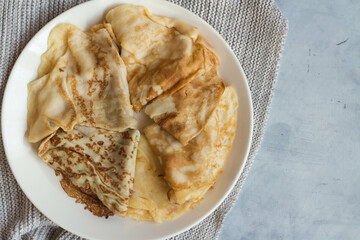 Pancakes are on a white plate on a gray knitted fabric