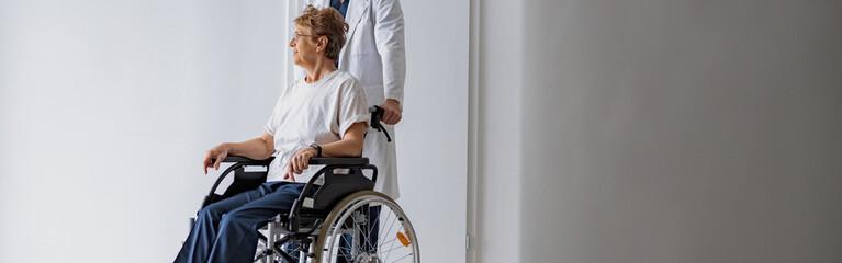 Fototapeta na wymiar Professional male doctor carrying patient on wheelchair in medicine clinic hall. High quality photo