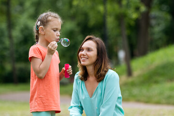 Girl with hearing aid blowing soap bubbles with mother.