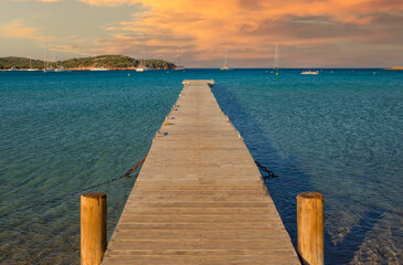 Brown wooden dock on turquoise blue sea during sunset at the Beach Rondinara.Scenic view of the blue sea and a long wooden dock at sunset at Rondinara beach, Corsica island, France