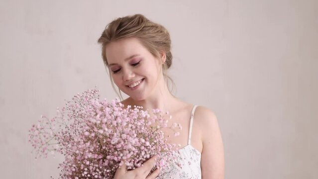 Beautiful woman in a dress at the window in a bright bedroom with a bouquet of pink spring gypsophila flowers.The concept of congratulations on womens day, the morning of the bride and valentines day.