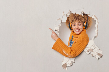 Cheerful surprised female repairer uses headphones for noise cancellation renovates apartment...