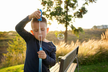 Niño pequeño chico infante latino rubio soplando y haciendo las burbujas jugando y disfrutando de...