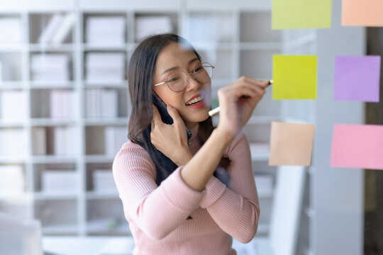 Asian businesswoman hand writing on sticky notes and talking on the phone. Business people meeting and writing share idea on sticky note.