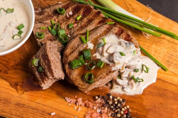 Rump steak on a wooden board with mushroom sauce. Quality beef. Barbecue season. Medium grilled steak.