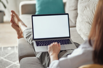 Mockup white screen laptop woman using computer lying on sofa at home, back view, focus on screen