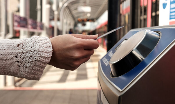 Female hand holding a card on contactless card reader machine in train station.