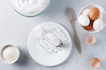 Whipped egg whites - whipped Italian meringue on a wire whisk, eggs, sugar, on a gray background.