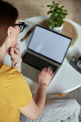 Mockup white screen laptop woman using computer while sitting at table at home, back view