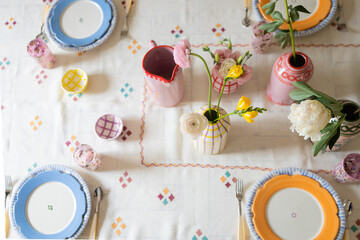 horizontal overhead shot of colorful ceramics and fresh flowers on embroidered tablecloth